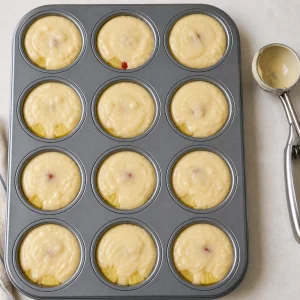Muffin cups filled with batter over pineapple and cherries.
