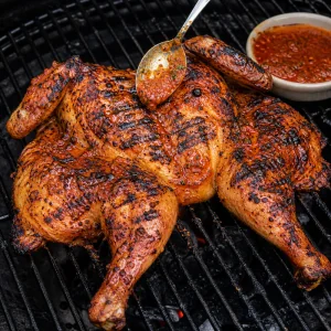 Browned piri piri chicken being sauced on the grill