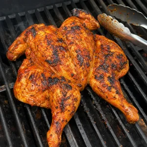 Turned piri piri chicken browning on grill grates with tongs nearby
