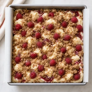 Unbaked coffee cake topped with raspberries and crumb mixture