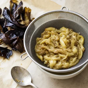 Tender roasted eggplant flesh draining in a mesh strainer