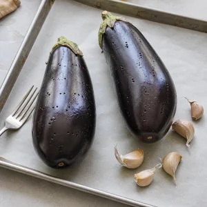 Whole eggplants pricked with a fork beside unpeeled garlic cloves