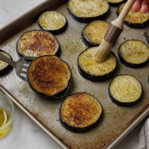 Roasted eggplant rounds being flipped and brushed with oil