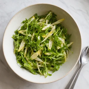 Fresh arugula and sliced endive lightly tossed with citrus vinaigrette in a mixing bowl