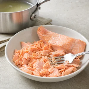 Cooked salmon flaked into bite sized pieces with a fork after poaching
