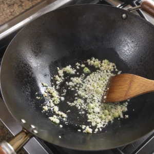 Parte bianca dei cipollotti e aglio tritato che sfrigolano nell'olio in un wok pulito