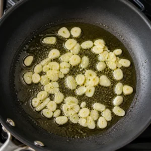 Thin garlic slices sizzling in olive oil in a skillet