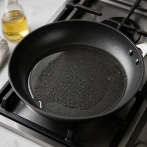 A non-stick skillet heating with a thin layer of vegetable oil for cooking cabbage pancakes.