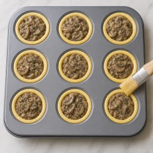 Filled mushroom tartelettes brushed with egg wash around the pastry edges.