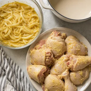 Drained marinated chicken beside a bowl of onions in marinade