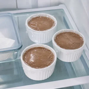 Ramekins of pate covered with plastic wrap and chilling in the refrigerator