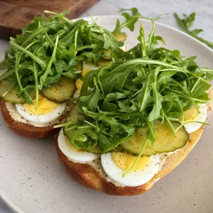 Pickles and fresh arugula layered over sliced eggs on open rolls