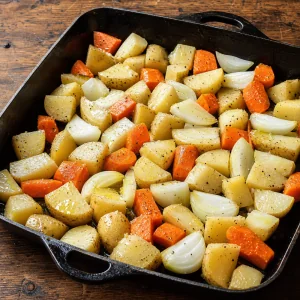 Potatoes carrots and onions tossed with olive oil in a roasting pan