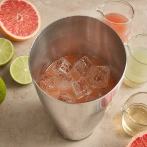 Grapefruit paloma mixture and ice in an open cocktail shaker