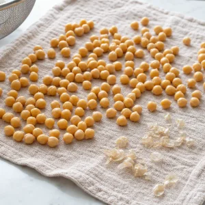 Kichererbsen trocknen auf einem Tuch neben gelösten Häutchen