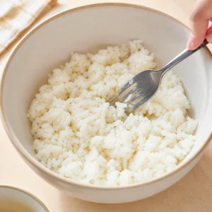 Cooked white rice loosened with a fork in a mixing bowl