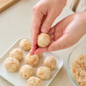Small chicken and rice balls being shaped by hand on a tray