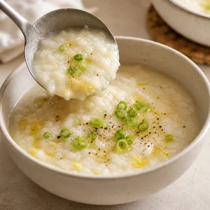 Ginger rice porridge ladled into a bowl with green onion garnish
