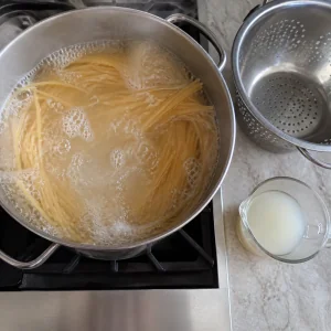 Spaghetti boiling in a large pot with reserved pasta water nearby.
