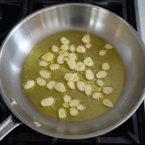 Thin garlic slices gently sizzling in olive oil in a wide skillet.