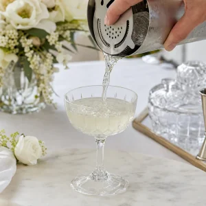 Gekuehlte Holunder-Gin-Mischung wird aus dem Shaker in das vorbereitete Coupeglas abgeseiht
