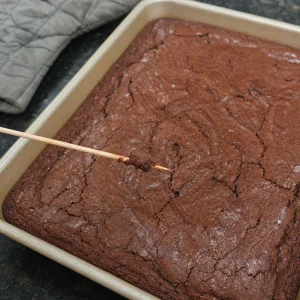 A toothpick checking baked brownies for moist crumbs.