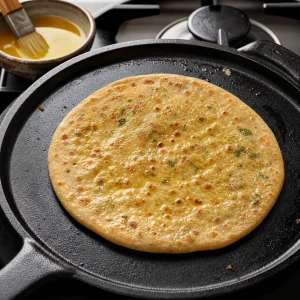 Partly cooked paratha brushed with ghee on a hot skillet.