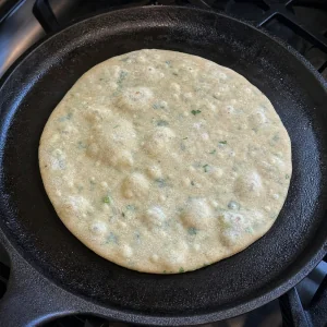 Uncooked paratha on a hot tawa with small bubbles forming.