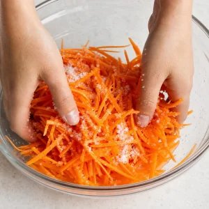 Salt and sugar being massaged into julienned carrots until they begin to soften.