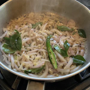 Onion, curry leaves, garlic, and green chile cooking in the pan