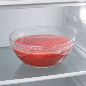Eine abgedeckte Schale mit Erdbeer-Passionsfrucht-Mischung kühlt auf einem Kühlschrankregal.