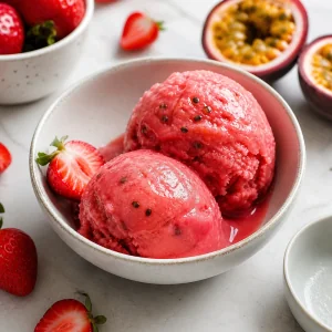 Zwei Kugeln Erdbeer-Passionsfrucht-Sorbet in einer Schale mit frischen Erdbeeren und Passionsfrucht.