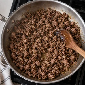 Agnello macinato e aglio tritato rosolano in padella mentre vengono sbriciolati con un cucchiaio.