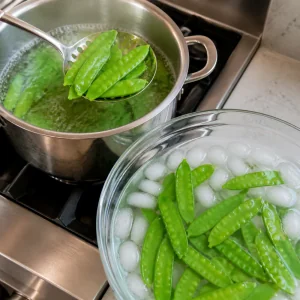 Snow peas lifted from boiling water into an ice bath