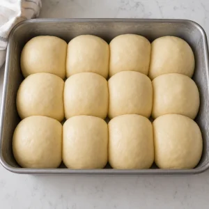 Doze bolas de massa fofas numa forma untada para a segunda fermentacao