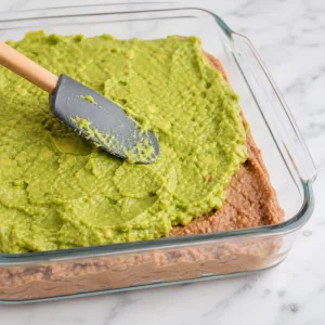 Guacamole being spread over the refried bean layer