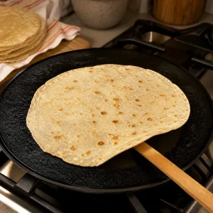 Lefse fino de patata cocinándose en una plancha caliente hasta que aparecen manchas doradas.