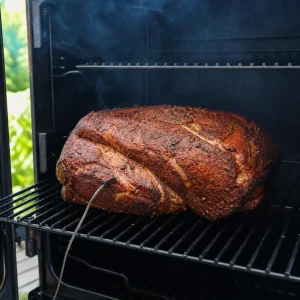 Seasoned pork shoulder smoking fat side up on the smoker grate