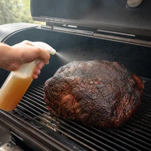 Smoked pork shoulder being spritzed with apple juice and cider vinegar