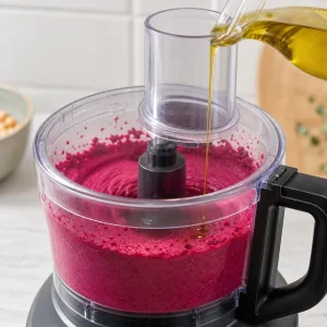 Olive oil drizzled into smooth magenta beet chickpea pâté in a food processor
