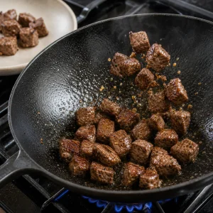 Browned beef cubes being tossed in a hot wok