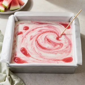 Marbled watermelon yogurt mixture swirled in a parchment-lined pan.