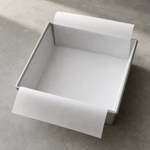 Square metal pan lined with parchment overhanging on two sides.
