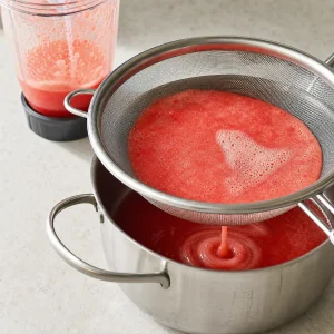 Watermelon purée draining through a fine sieve into a saucepan.