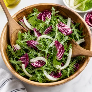 Arugula, radicchio, and fennel tossed together in a large wooden salad bowl