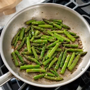 Morceaux d’asperges cuisant dans une poêle jusqu’à être vert vif et tendres-croquants.