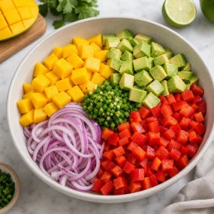 Diced mango, avocado, red bell pepper, red onion, and jalapeño combined in a salad bowl.