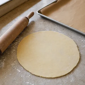 Pie dough rolled into a round beside a rolling pin
