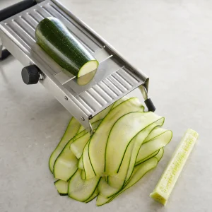 Thin zucchini ribbons beside a stainless-steel mandoline